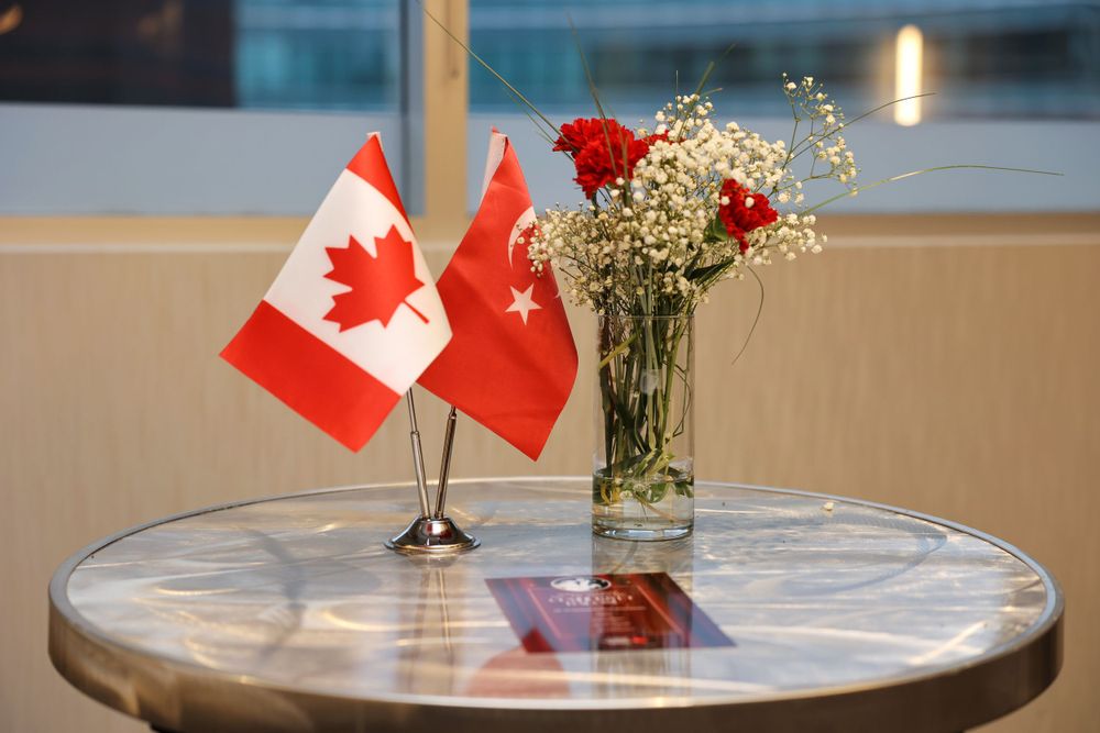 Turkish and Canadian flags displayed on a round table with red carnations and baby's breath in a glass vase.