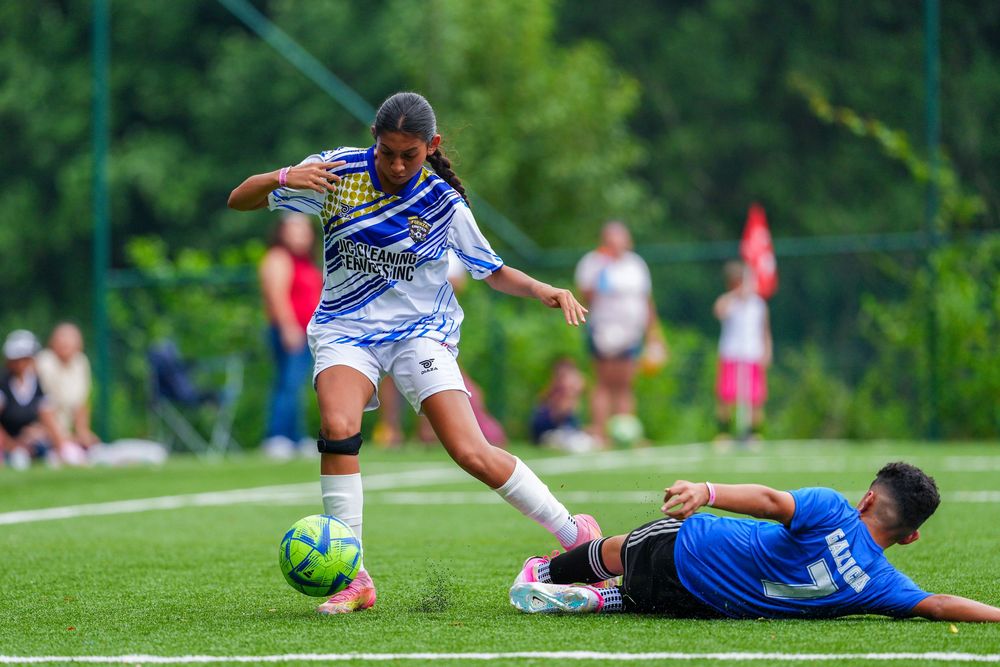 Two female soccer players compete for the ball on a green turf field during an outdoor youth soccer match.