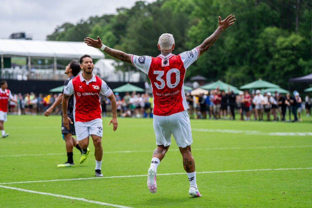 Soccer player number 30 in red and white kit celebrates goal with arms raised on green field.