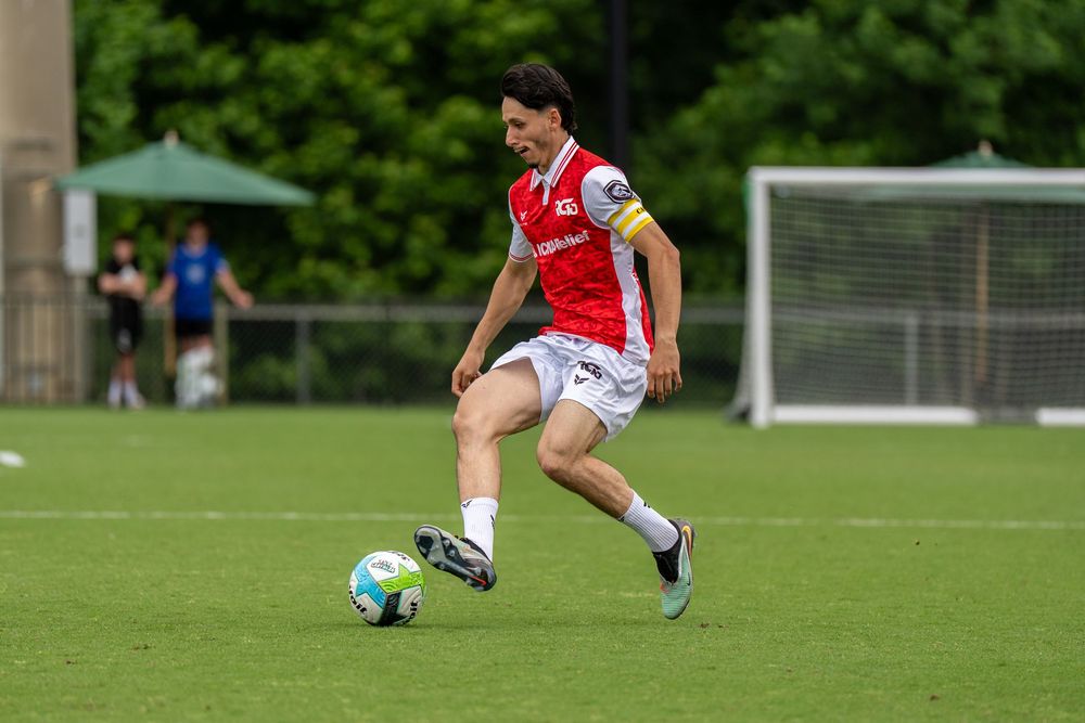 Soccer player in red and white uniform dribbling ball on green field during match.