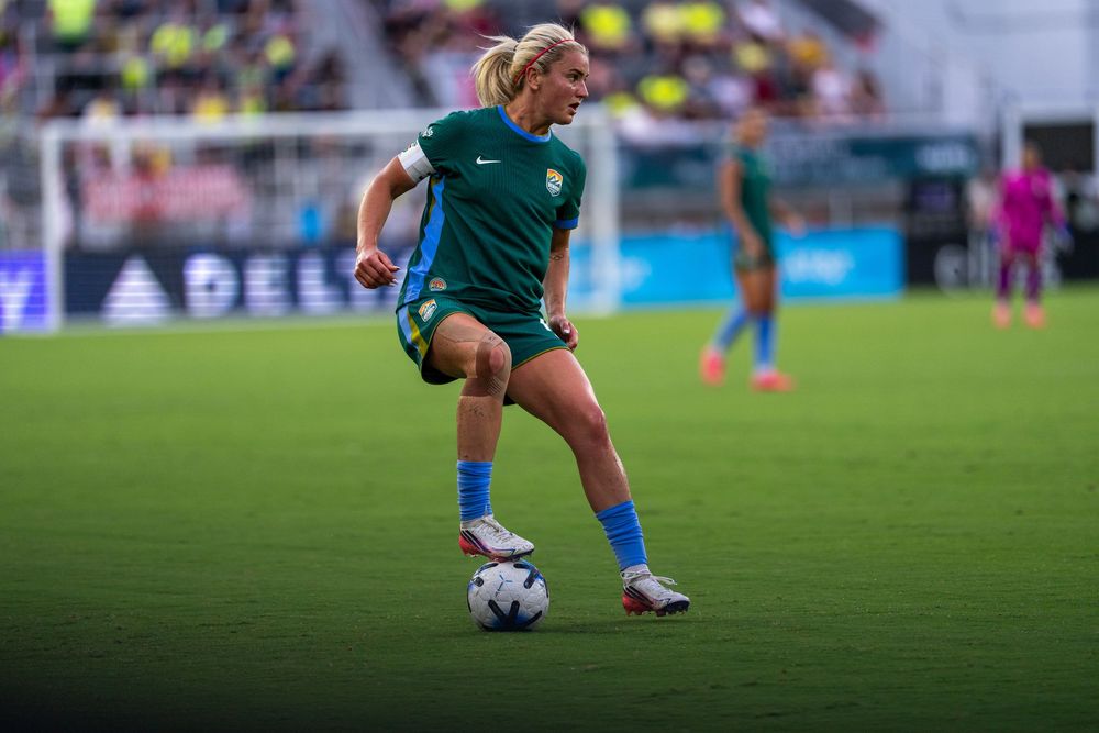 Female soccer player in green kit dribbling ball on stadium pitch during professional women's football match.
