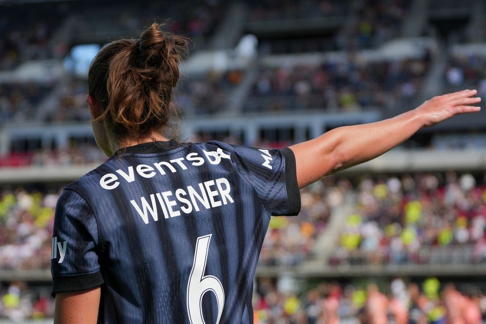 Soccer players in dark jerseys celebrate during a match with one player wearing number 6 on their back.