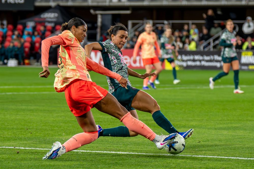 Two soccer players battle for possession of the ball during a competitive match under stadium lights.