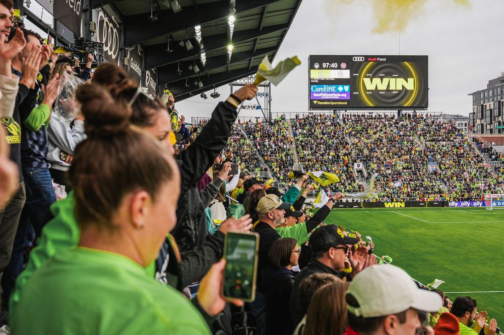 Packed stadium crowd watching a sporting event with spectators filling the stands and field during daytime.