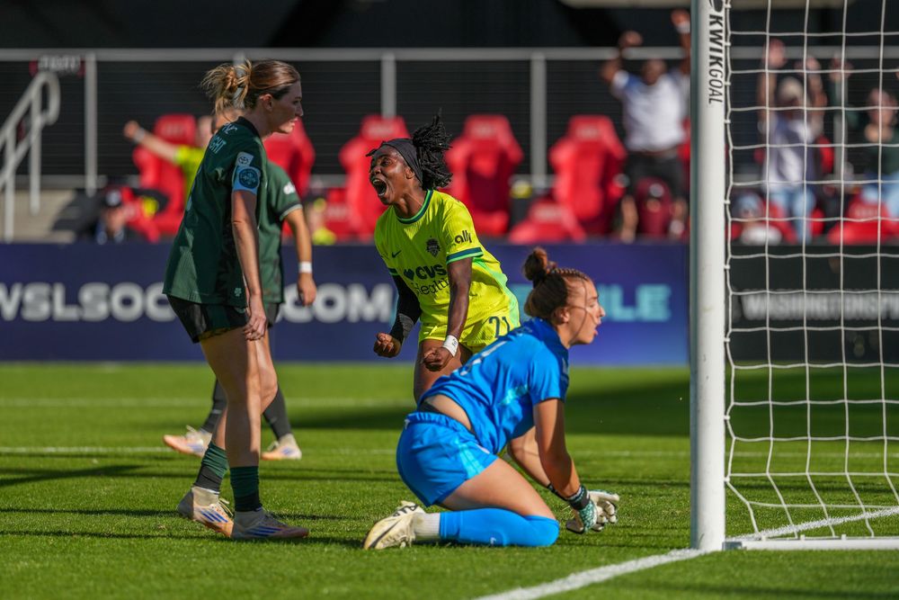 Soccer goalkeeper in blue uniform sits dejected on ground near goal post during match.