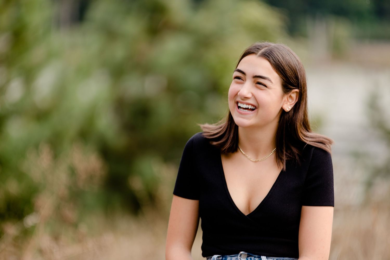 A joyful expression and genuine laughter while wearing a black v-neck t-shirt outdoors with greenery in background.