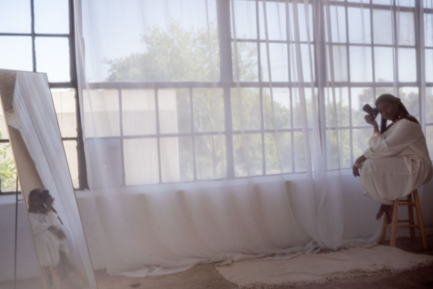 Photographer taking a dreamy portrait in bright sunlit room with billowing white curtains and natural window light.