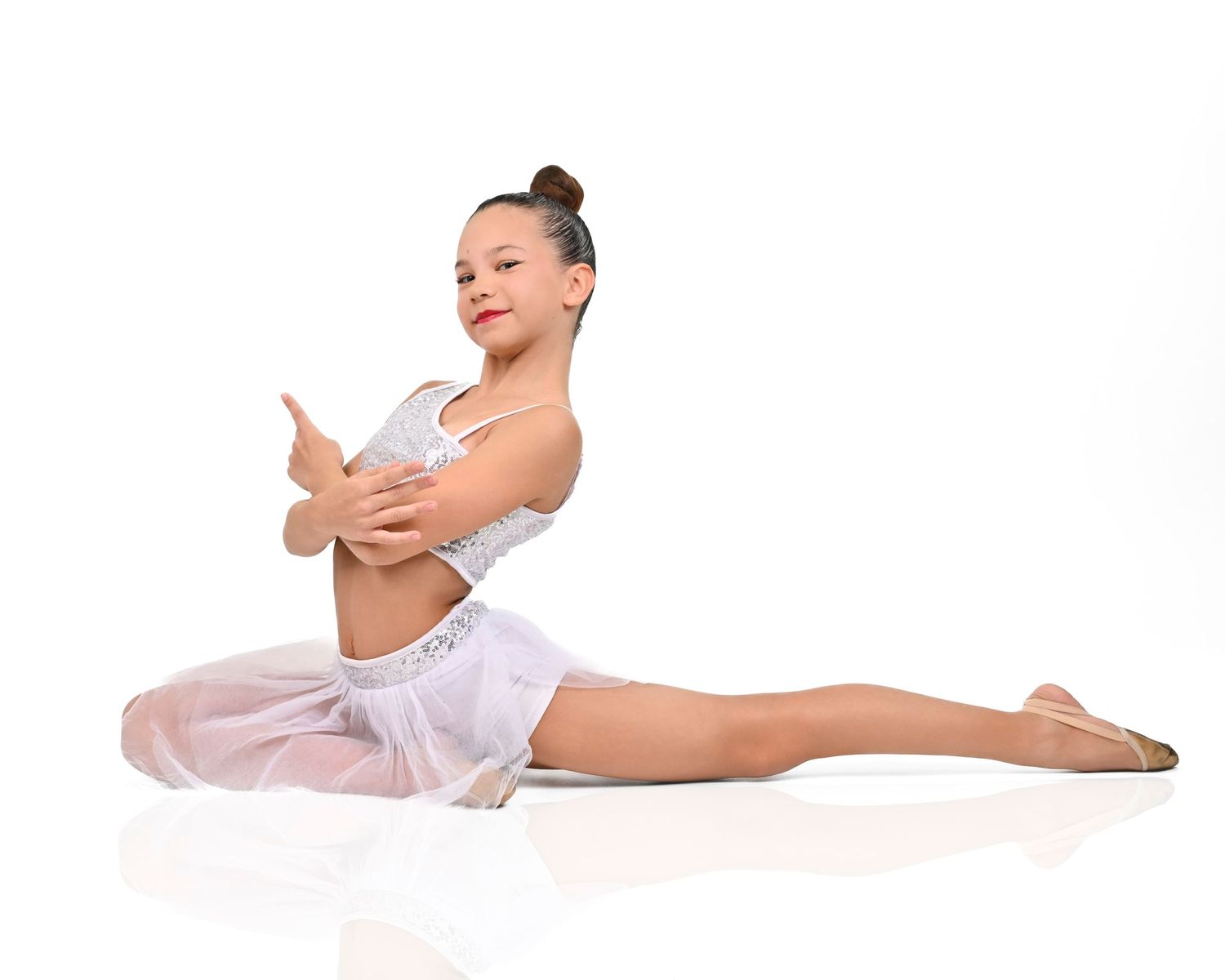 Young ballet dancer in white costume performs graceful pose on floor during dance recital.
