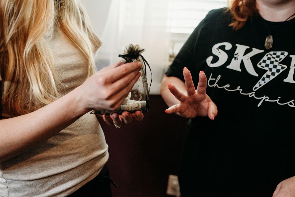Two women examining a small creature in a glass jar, one wearing a ski therapist shirt.