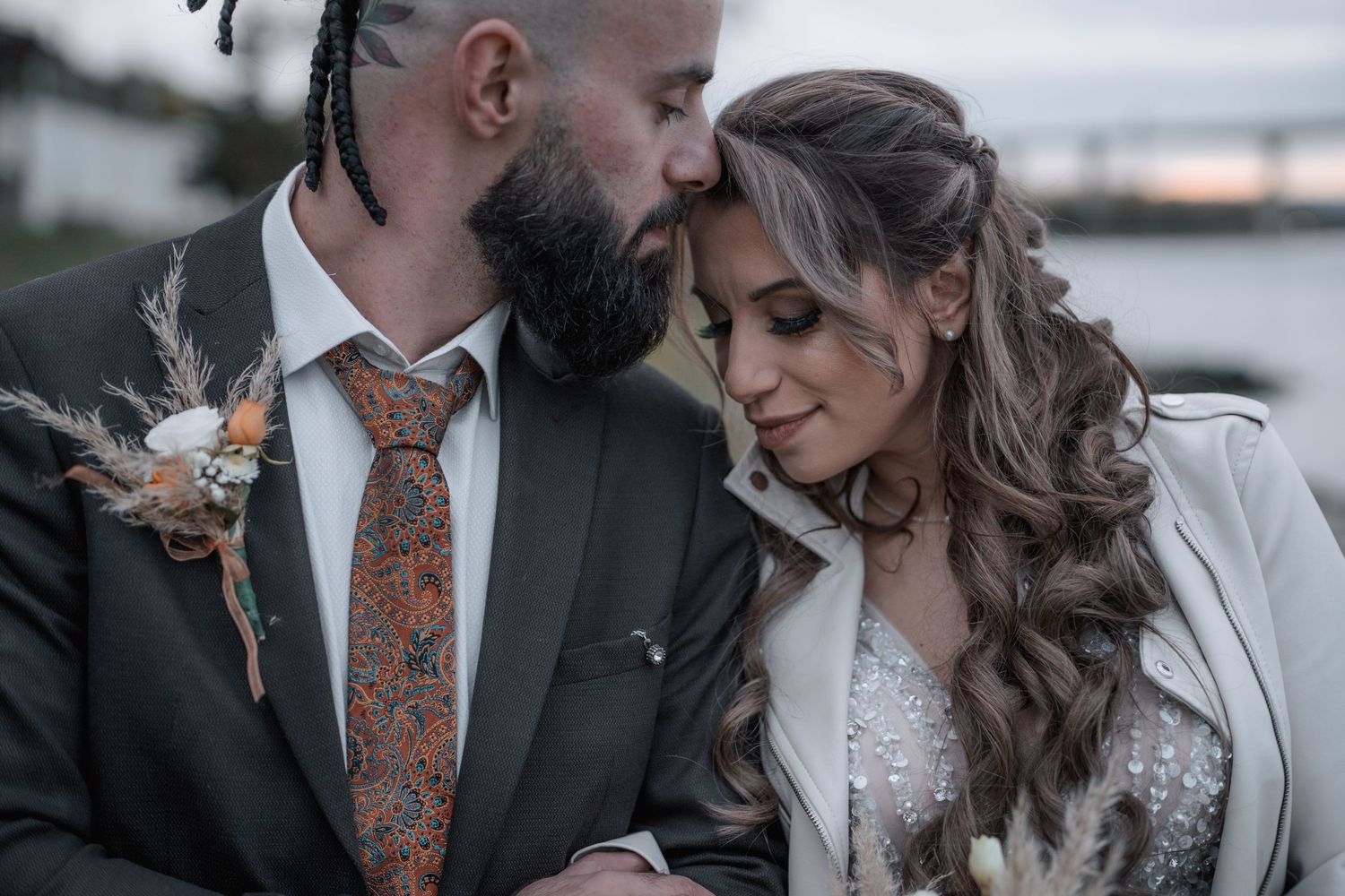 Romantic wedding couple in moody lighting share intimate moment by waterfront.