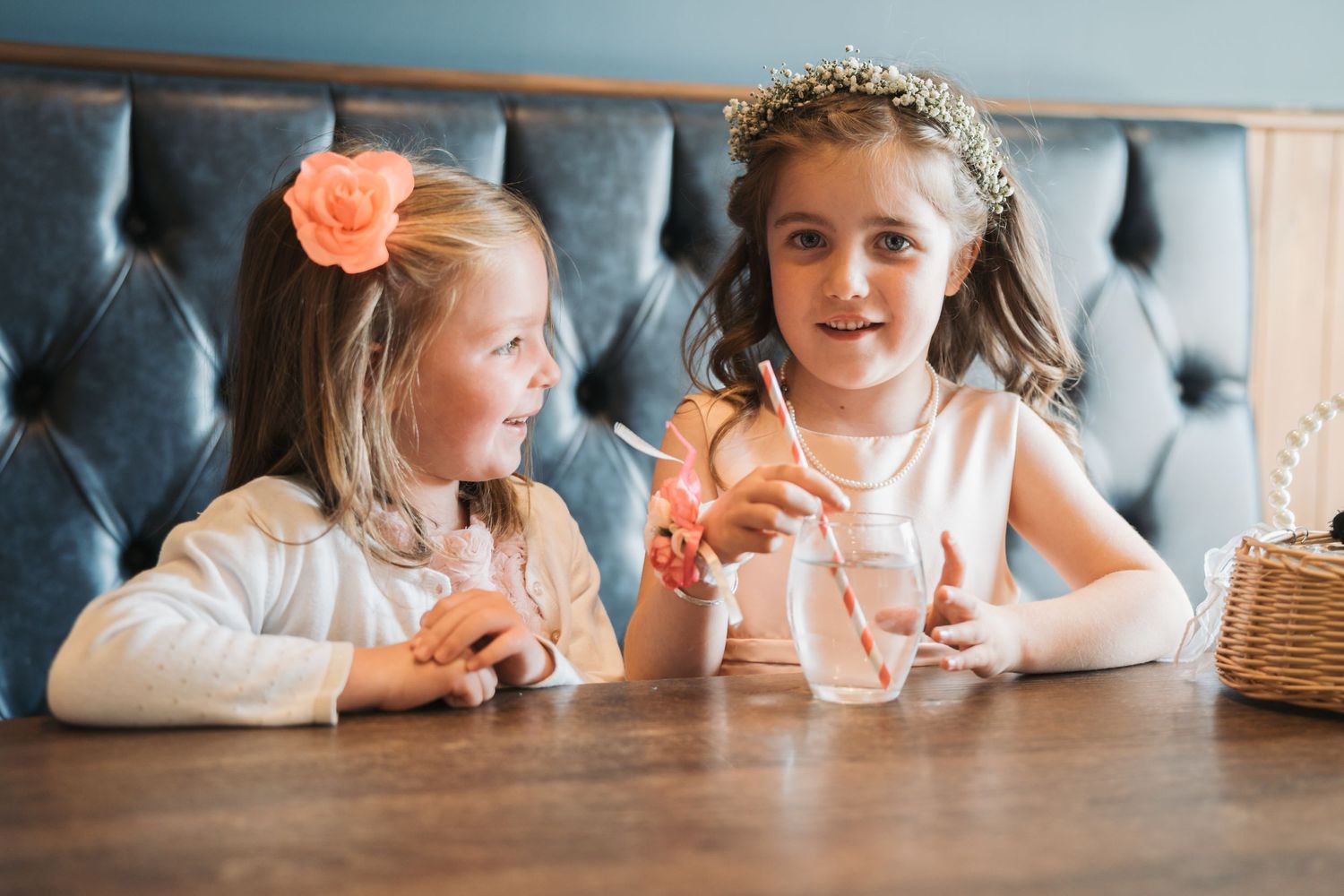 Two children enjoying milkshakes together at a restaurant booth with upholstered gray seating.