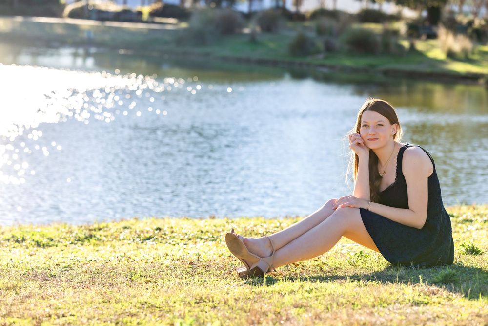 A person relaxes on grassy lakeside while reading a book on a sunny afternoon.