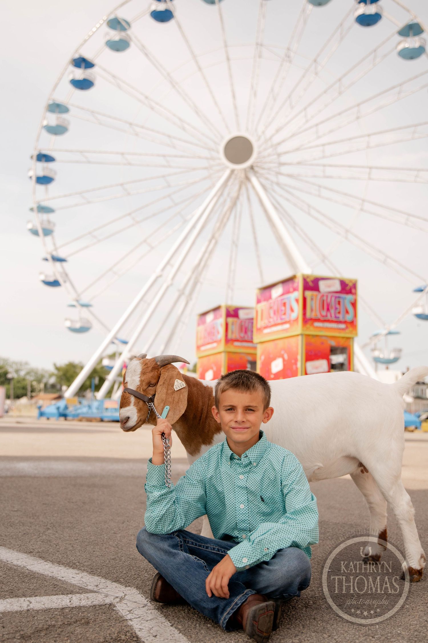 Goat and exhibitor pose in front of a ferris wheel at a county fair.