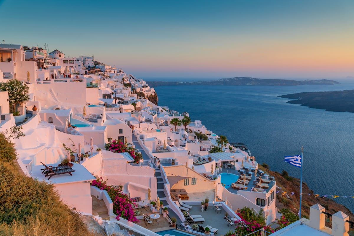Stunning sunset view of white-washed buildings cascading down the cliffs of Santorini, Greece overlooking the Aegean Sea.