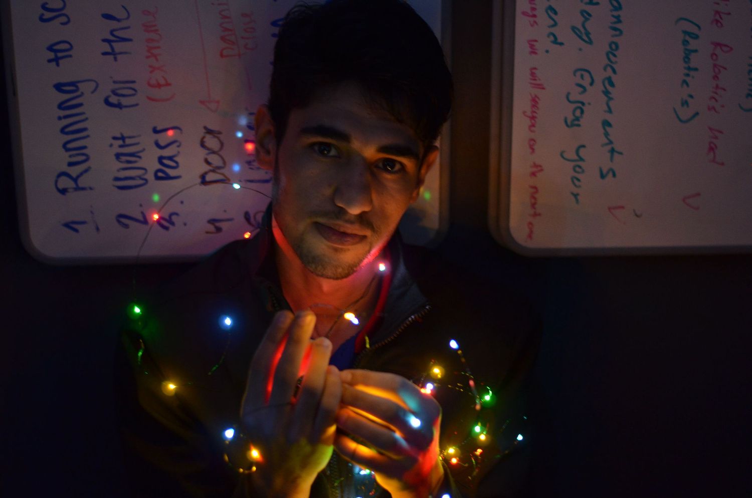 Someone holds a drink while illuminated by colorful Christmas lights in a darkened room.