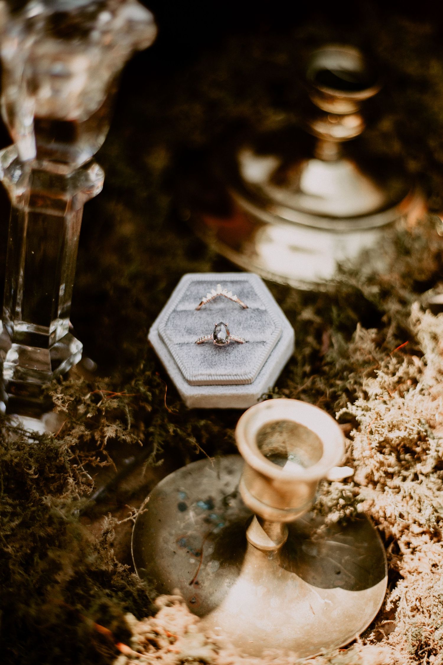 Wedding ring displayed in hexagonal box with vintage candlesticks and moody lighting.
