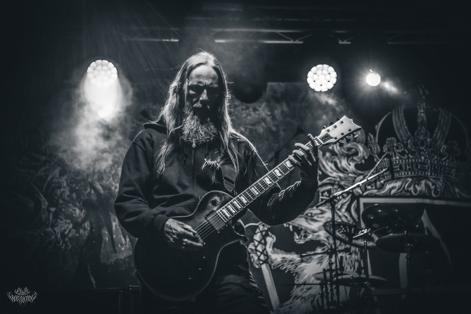 Black and white photo of guitarist performing on stage with dramatic backlighting and fog.