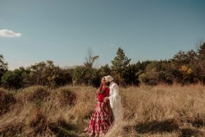A romantic couple embraces in a golden autumn field with tall grass and evergreen trees under a blue sky.