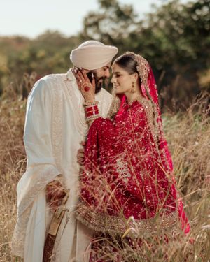 A romantic couple in traditional South Asian wedding attire share an intimate moment in a field during golden hour.