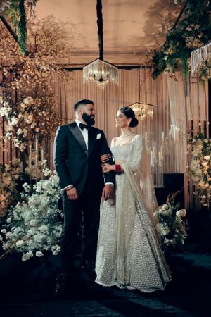 A couple poses at their elegant wedding ceremony with floral decorations and soft lighting in an indoor venue.