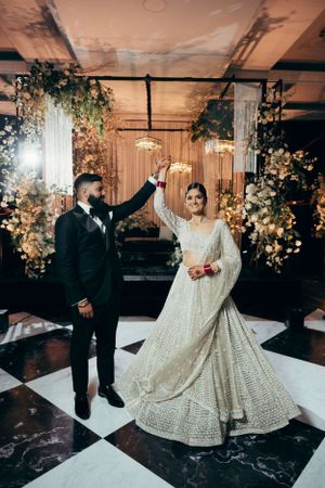 A newlywed couple dances on a black and white checkered floor surrounded by romantic floral arrangements.