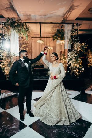 A couple dance at their wedding reception with elegant floral decor and a black and white checkered dance floor.