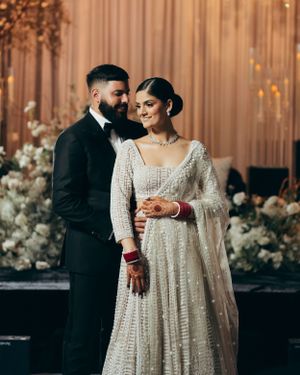 A couple shares an intimate moment at their wedding reception with white floral decor and a champagne-colored backdrop.