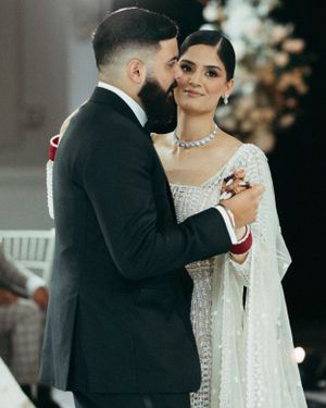 A couple shares an intimate moment during their first dance, with the bride in a sparkling white gown and groom in black suit.