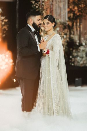 Newlyweds share a romantic dance together, the bride in an elegant white cape dress and groom in classic tuxedo.