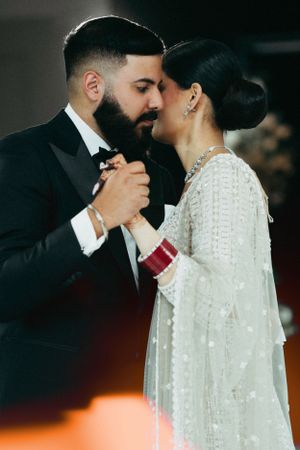 A wedding couple embraces during their formal dance, with bride in white beaded dress and groom in tuxedo.