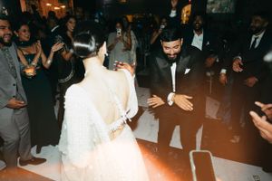 A couple dances together on an illuminated dance floor at a wedding reception surrounded by guests.