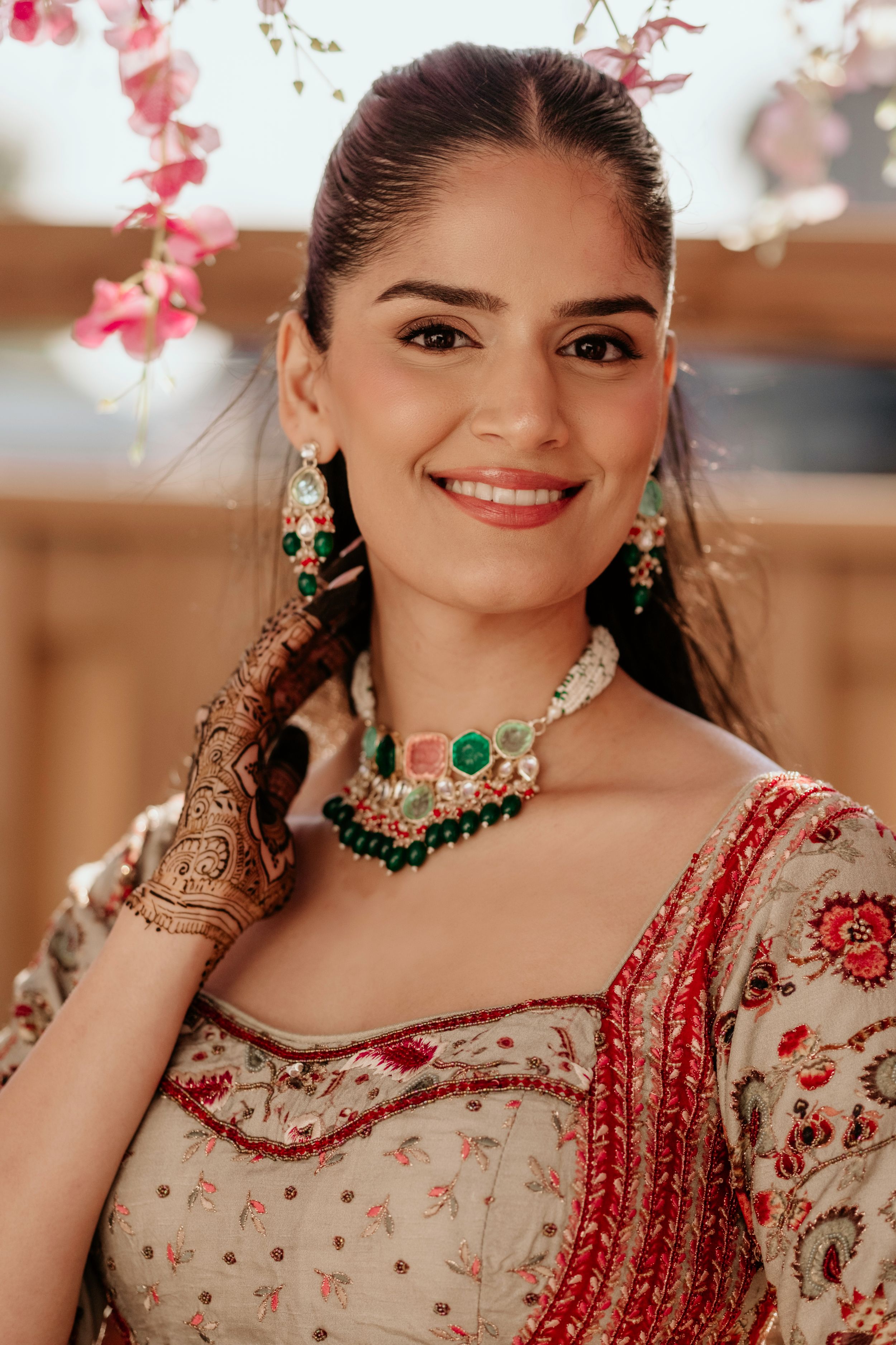A beautiful portrait showcasing traditional Indian bridal jewelry and henna adorned hands with a red and cream lehenga.