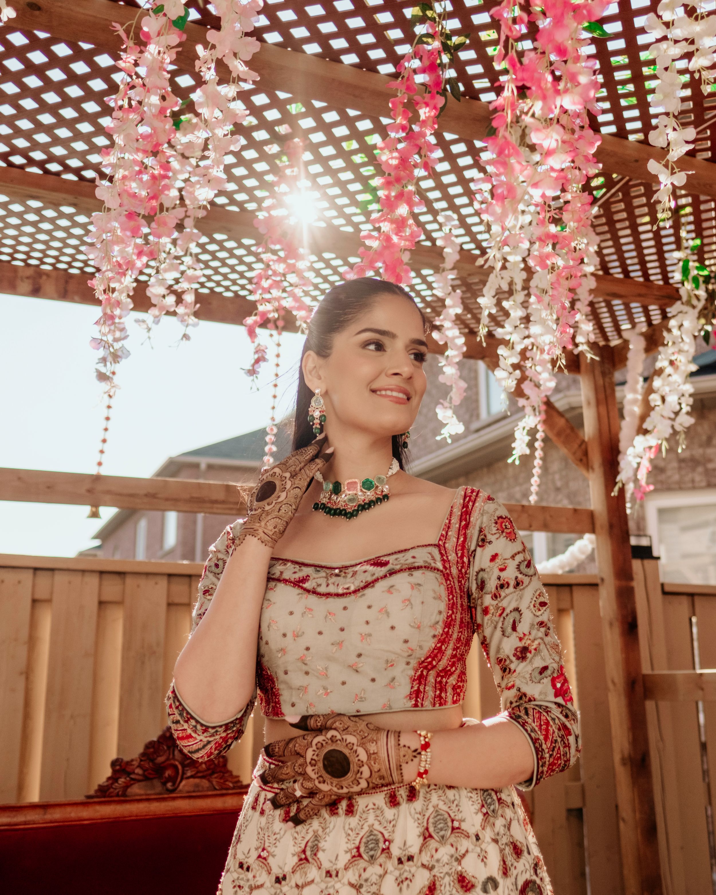 Beautiful traditional Indian bridal outfit with delicate embroidery under a pergola decorated with pink floral garlands.