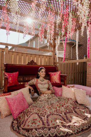 Elegant wedding decor features hanging pink floral garlands and draped fabrics above a luxurious seating area with red cushions.