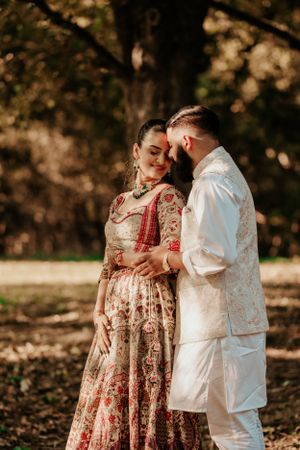 Romantic outdoor couple portrait with traditional Indian wedding attire against a natural autumn backdrop.