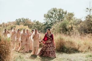 Wedding party walking through an autumn field with the couple leading and bridesmaids in beige dresses following behind.
