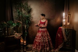 Traditional Indian bridal attire in rich red lehenga with intricate embroidery shown in moody, atmospheric indoor setting.