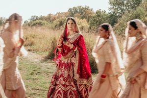 Beautiful traditional Indian bridal party outdoors with bride in red lehenga surrounded by bridesmaids in light peach outfits.