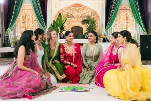 A festive gathering of people wearing colorful traditional Indian saris and lehengas sit together during a celebration.