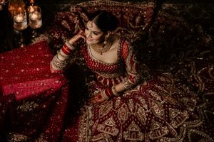 A traditional Indian bridal lehenga in deep red with intricate gold embroidery captured in dramatic low light.