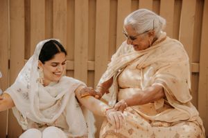 Two people in traditional South Asian attire share an intimate moment while seated together against a wooden backdrop.