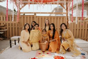 A group in traditional South Asian attire sits together at a festive celebration decorated with pink streamers and flowers.