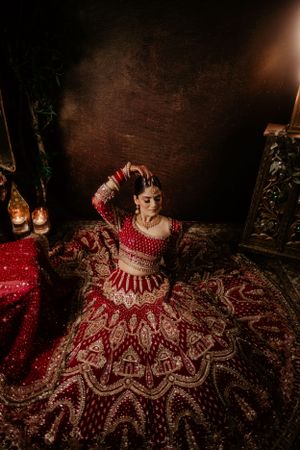Moody portrait of traditional Indian bridal attire featuring an intricate red and gold lehenga in dim lighting.