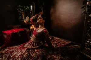 A person in a luxurious red traditional Indian bridal lehenga poses dramatically in moody lighting.