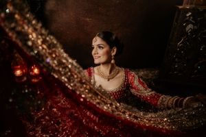 A traditional South Asian bride wearing an ornate red lehenga with intricate gold embroidery in dramatic lighting.