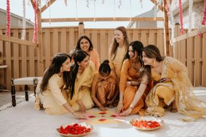 A group in golden yellow dresses gather around a platter of fresh fruit on a covered patio area.