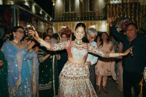 A dancer in a traditional Indian lehenga twirls at a festive celebration with string lights and guests in the background.