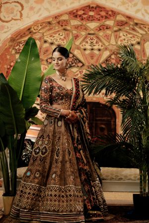 Traditional Indian bridal lehenga with intricate beadwork and embroidery shown against ornate backdrop with tropical plants.