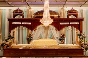 An elegant wedding mandap stage with crystal chandelier and draped fabric decorations in cream and burgundy.
