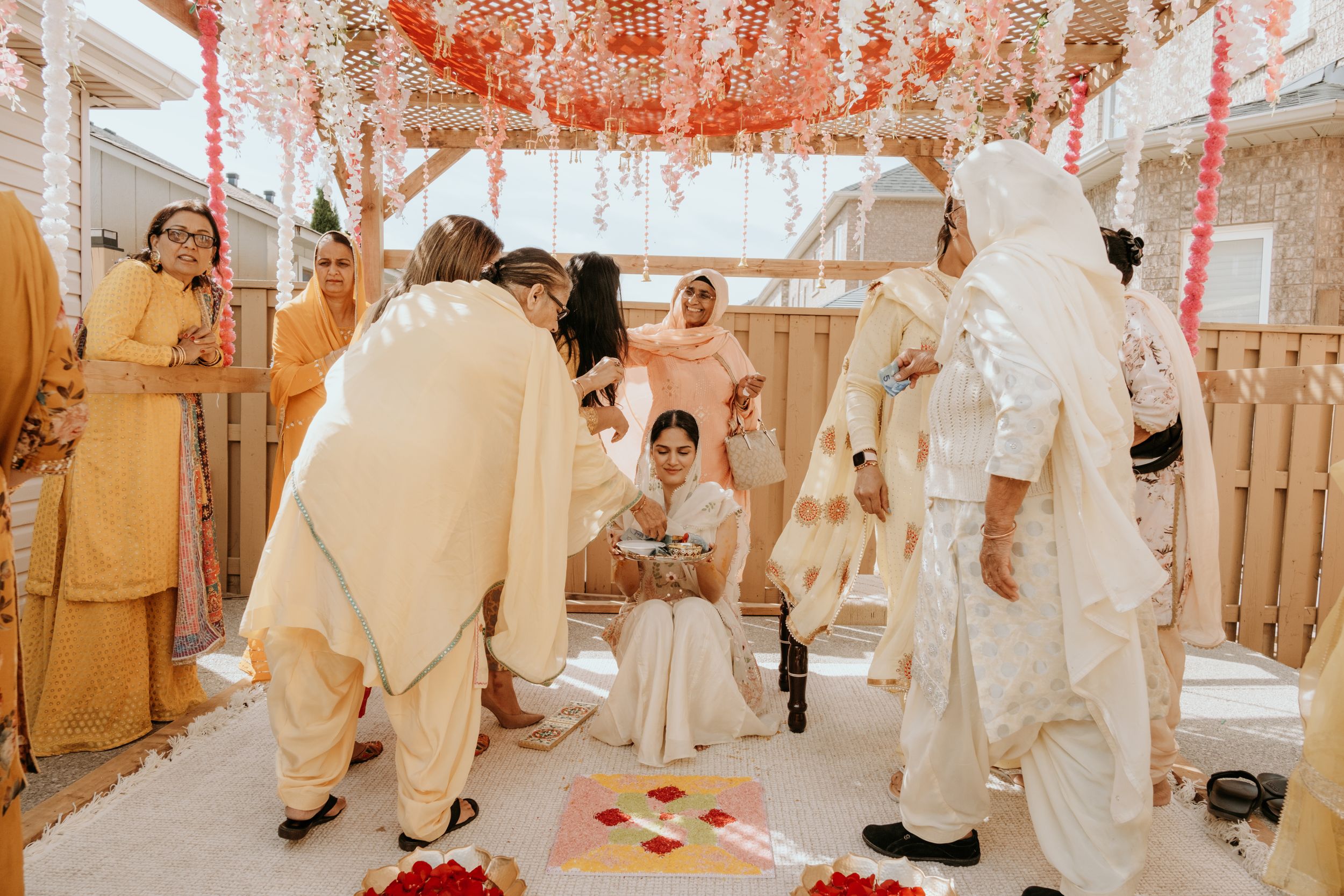 Traditional wedding ceremony with guests gathered under an ornate orange and white tent canopy during a cultural celebration.